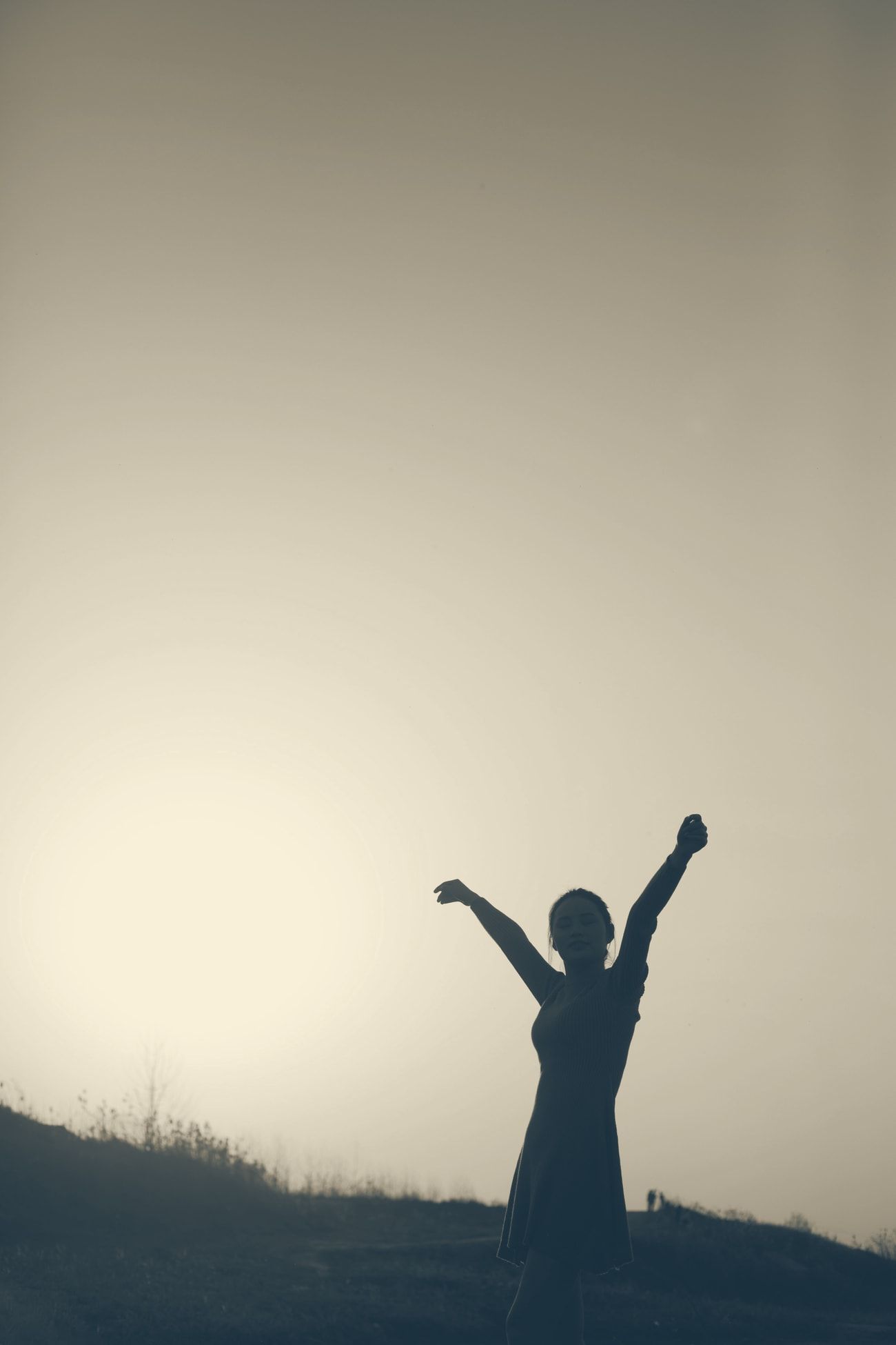 A person raising their arms toward a glowing sky at sunset.